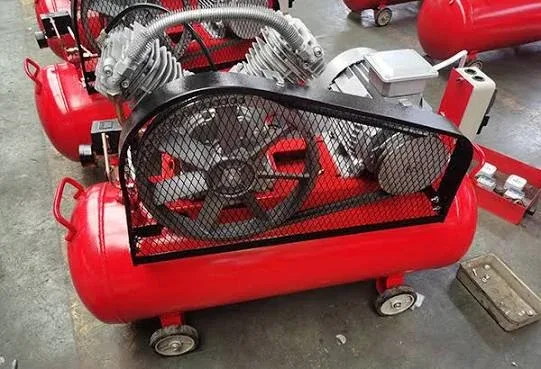 Red wheel-mounted belt-driven piston air compressor with guard in a factory